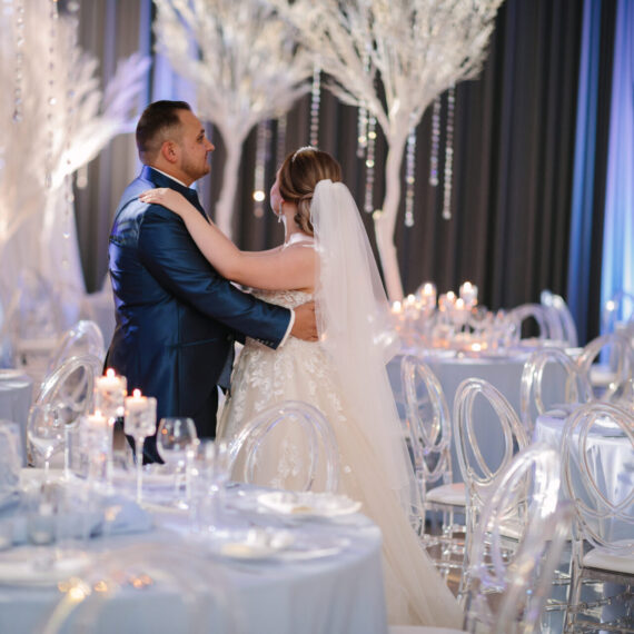 In dieser Hochzeitsfotgrafie sieht man das Brautpssr bei dem Hochzeitstanz in der Hochzeitslocation. Die Hochzeitsdekoration wurde in Blau und Weiß Tönen und im Winter-Stil dekoriert. Platzteller, Tischdecken Tischnummern, Kerzen.