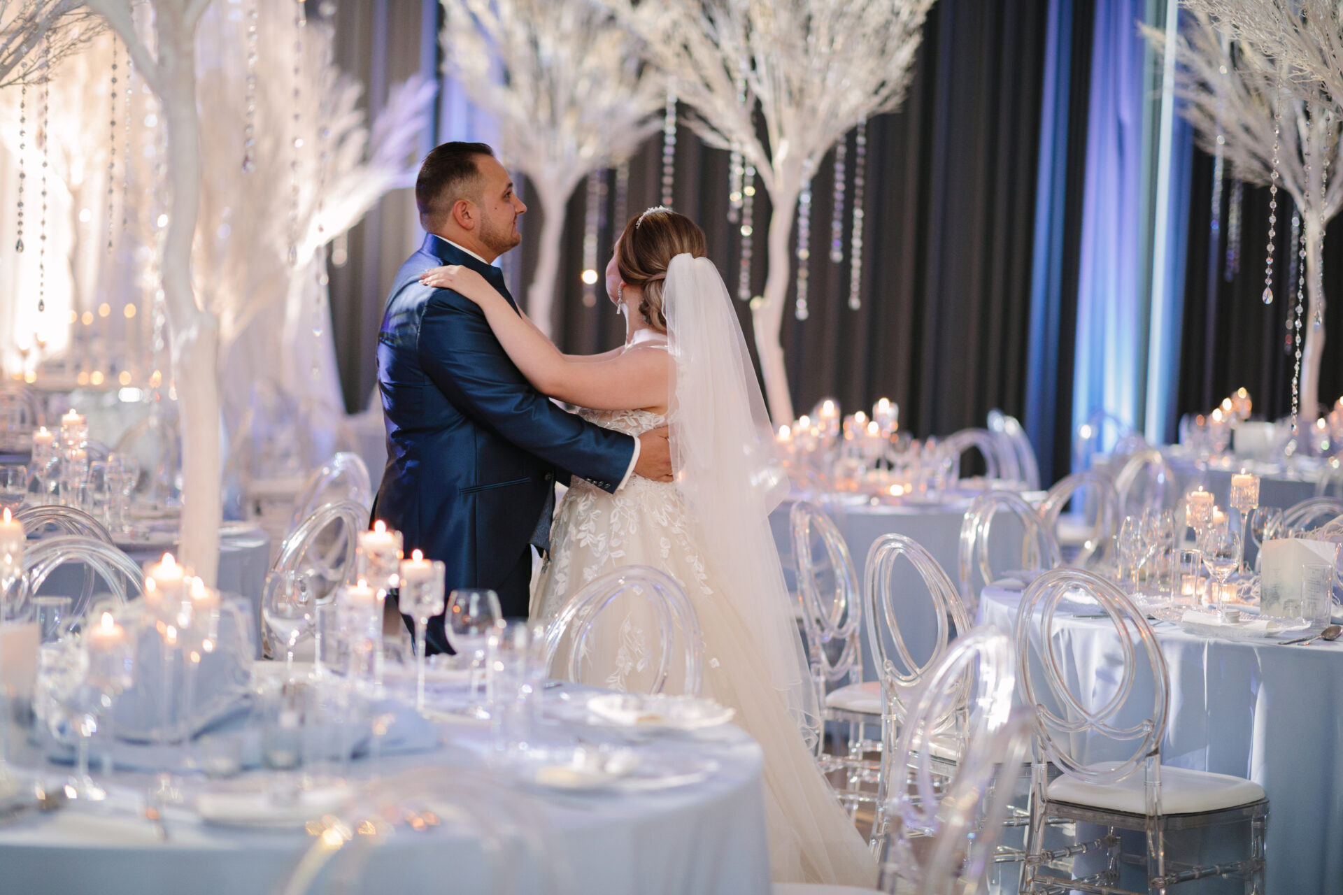 In dieser Hochzeitsfotgrafie sieht man das Brautpssr bei dem Hochzeitstanz in der Hochzeitslocation. Die Hochzeitsdekoration wurde in Blau und Weiß Tönen und im Winter-Stil dekoriert. Platzteller, Tischdecken Tischnummern, Kerzen.